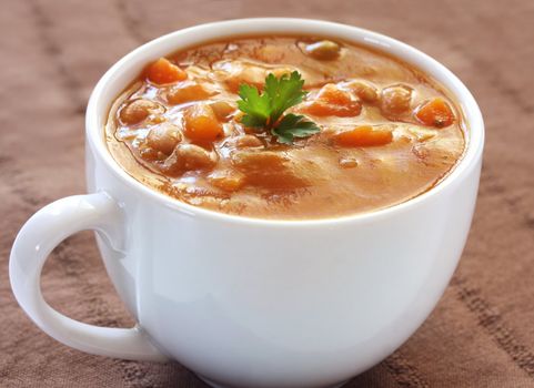 Cup of hearty vegetable soup, on brown cloth.