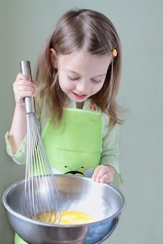 Little girl uses an extra large whisk to beat eggs for breakfast. Some motion blur on whisk where little girl is beating eggs.