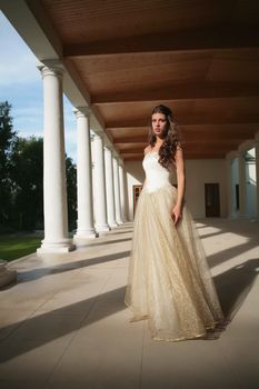 solar evening in gallery of the old-time building, girl in luxurious white-golden gown