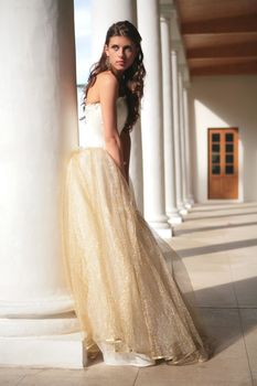 girl in white-golden gown of the bride amongst colonnades of the old-time building