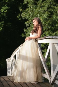 beautiful girl in gown of the bride on white bridge through river beside entry in park