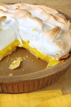 Home-baked lemon meringue pie, in brown pottery pie plate.  One slice missing.