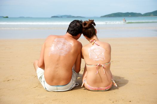 Young couple enjoying the beach with an heart draw on their backs