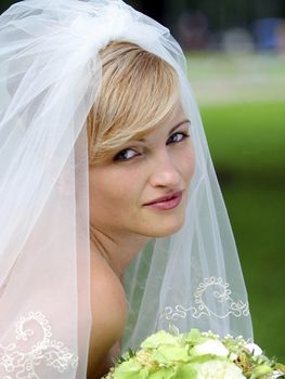 Smiling bride in white with veil and bouquet of flowers.
