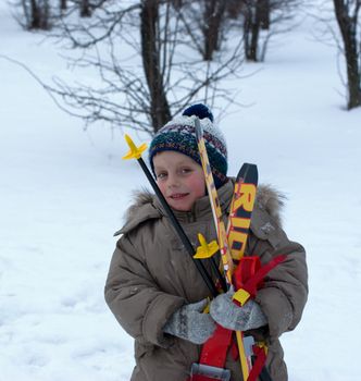 The smiling boy walks with skis