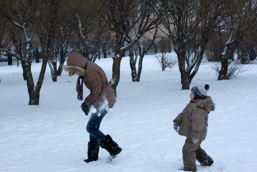 The boy with mother play snowballs in snow-covered park