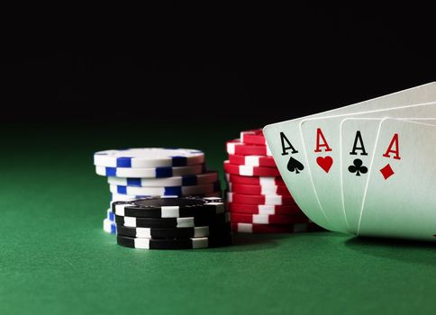 four aces high on green table with chips on black background
