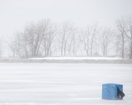 An ice fishing tent on a lake during a winter snow storm.