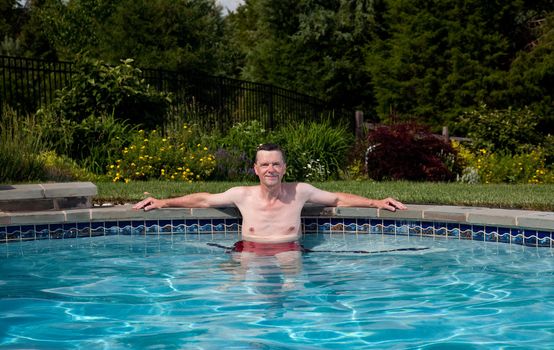 Man in his fifties relaxing in a pool in a backyard garden
