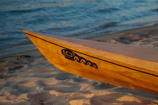 Sunset rays hitting the polished wooden bow of a kayak on a beach by the ocean