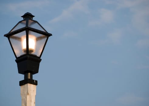 A lit up street light against a blue sky.