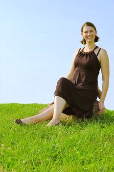 Smiling girl sitting on stone on blue sky