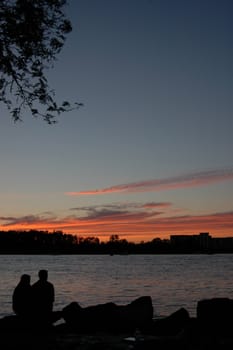 A couple sitting beside a river watching the sun set.