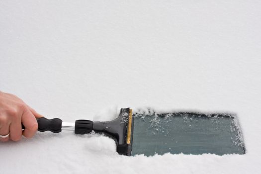 hand with an ice scraper cleaning a windshield