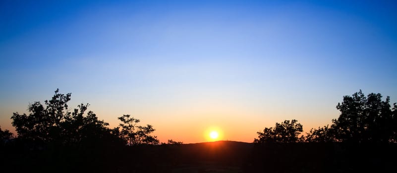 wounderful sunset with sun and siluet of trees and mountains