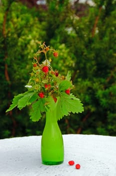 Some strawberries in av vase, standing on a table in a garden.