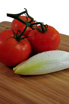 Thre tomatoes and Endive on a wooden cutting board.