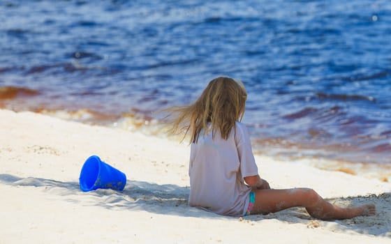 Young girl playing in the sand at the beach blue water and blue bucket 