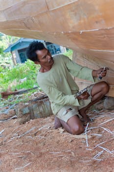 Indonesian Boat Builder working on a wooden boat with hand tools