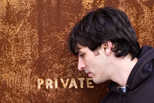 A young man standing outside an old door or entrance that reads PRIVATE.  A great image for any identity theft concept.