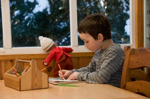 boy drawing a picture with his doll nearby
