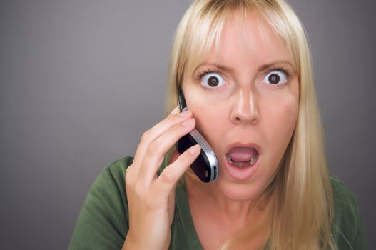 Stunned Blond Woman Using Cell Phone Against a Grey Background.