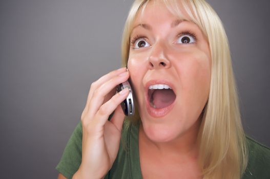 Stunned Blond Woman Using Cell Phone Against a Grey Background.