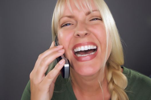 Joyful Blond Woman Using Cell Phone Against a Grey Background.