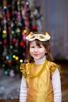 Girl wearing carnival mask and golden dress near xmas tree
