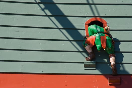 Wooden made jester seems to climb hrough a window