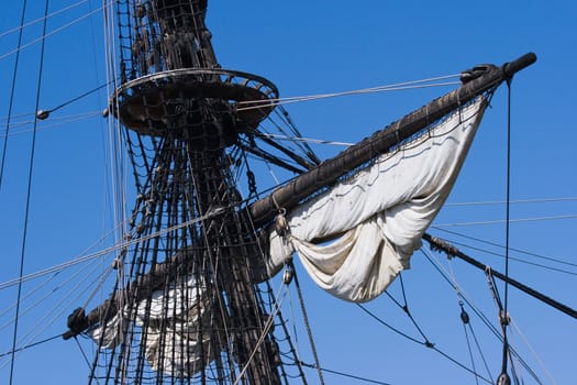 Mast, ropes and sails from old sailingship on a blue sky background