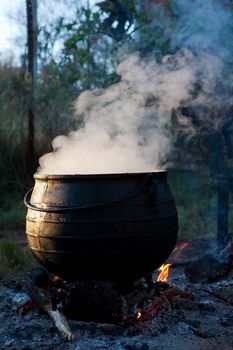 black cast iron pot boiling on a fire with steam pouring out of the top