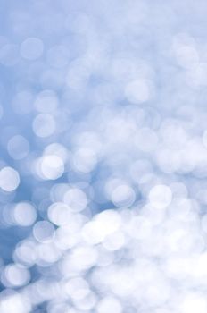 Out of focus bokeh background of blue water with sun reflections. Can be used as Christmas or winter backdrop.