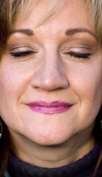 A pretty middle aged woman smiling with her eyes closed.  Shallow depth of field.