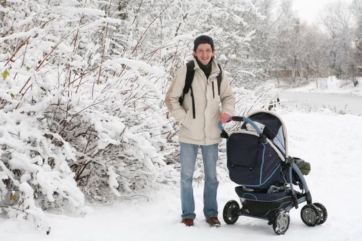 smiling man in light jacket and with perambulator in park after snowfall