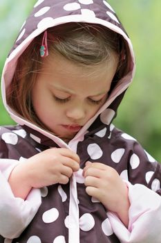 Little girl dresses herself in a raincoat.