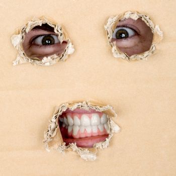 Eyes and teeth look out from hole in cardboard