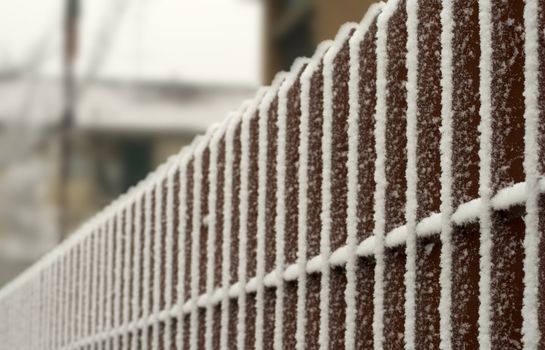 Snow on red vertical bars of an iron fence