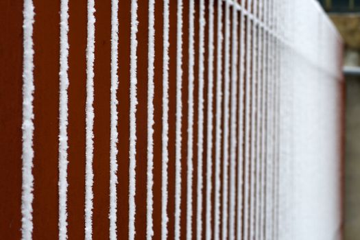 Snow on red vertical bars of an iron fence