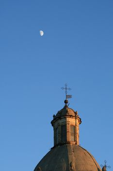 The moon in daylight over the dome of a church