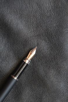 Fountain pen lying on black leather background with copy space