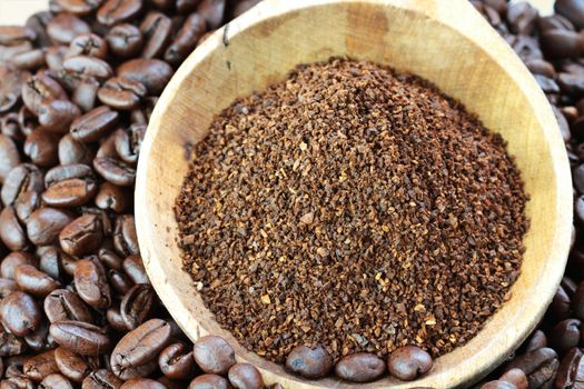 Coffee beans and ground coffee in a wooden spoon. 
