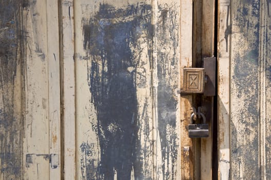 Detail of old door with a bolt. Metal and peeling paint. Padlock.