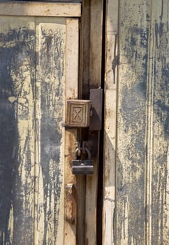 Detail of old door with a bolt. Metal and peeling paint. Padlock.