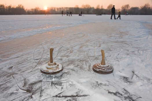 two curling stones on a frozen lake at sunset