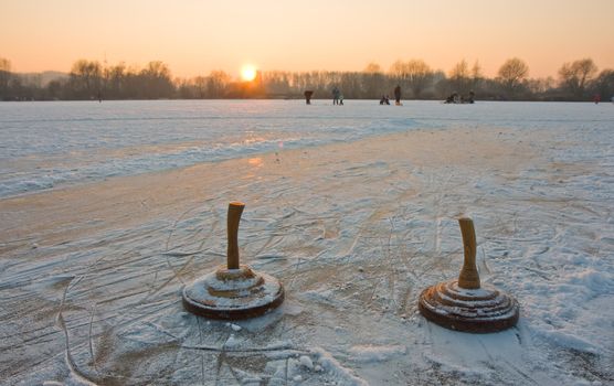two curling stones on a frozen lake at sunset