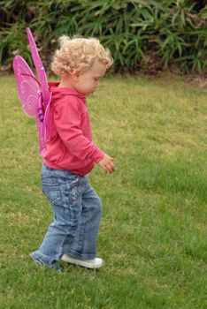 Child blondie girl with short hair and butterfly costume wings walking on the grass.