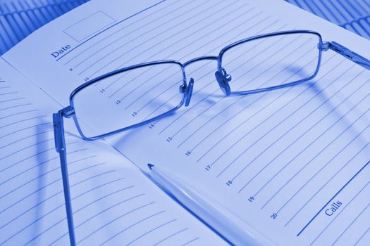 Glasses, pen and notebook, photographed close up.