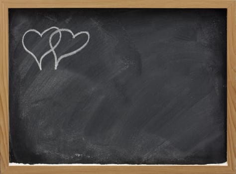 blackboard in wooden frame with eraser smudges and two interlaced hearts sketched with white chalk in a corner, copy space