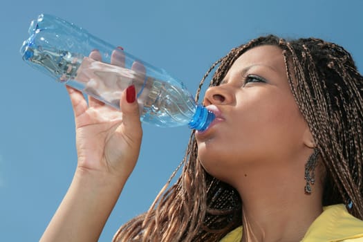 close-up, black girl drinks a water from plastic bottle on background blue sky